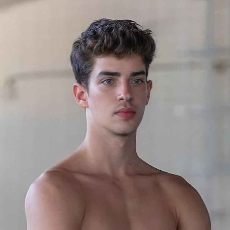 A close-up, smiling portrait of Manu Ríos, showcasing his signature cute and stylish aesthetic. He is looking directly at the camera with his striking green eyes, against a neutral background that highlights his sharp features and modern fashion sense.
